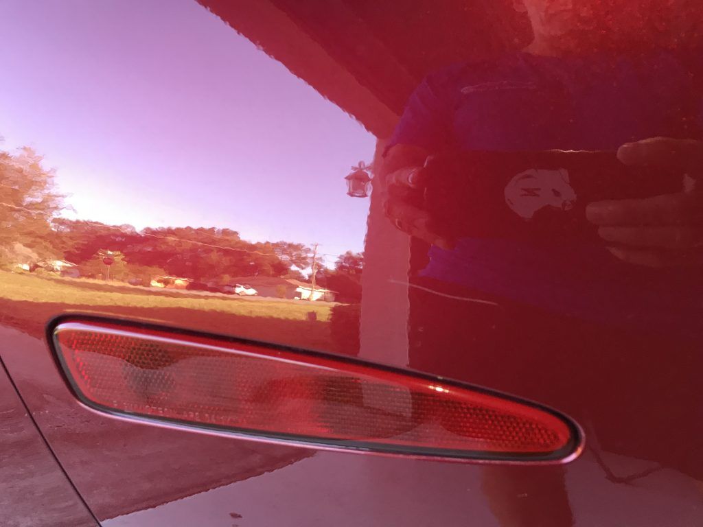 A person is taking a picture of their reflection in a red car