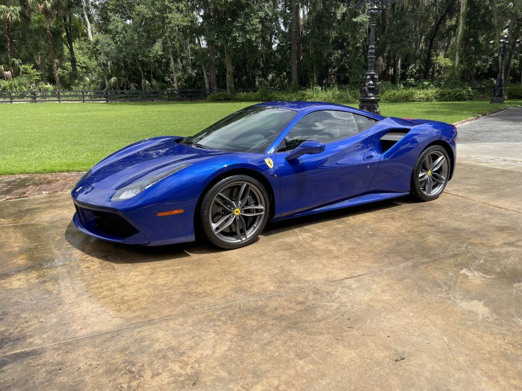 A blue ferrari 488 spider is parked in a driveway.