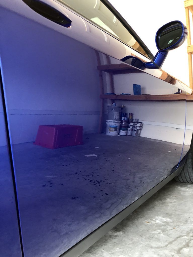A blue car is parked in a garage next to a shelf.