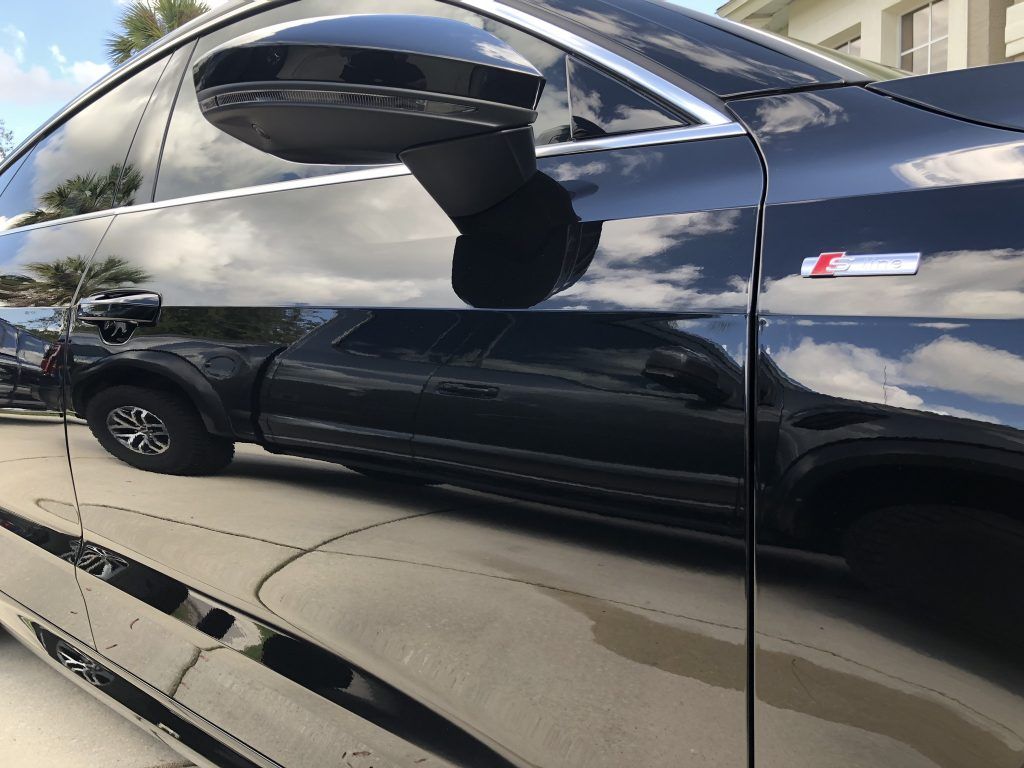 A black car is parked in a driveway next to a building.