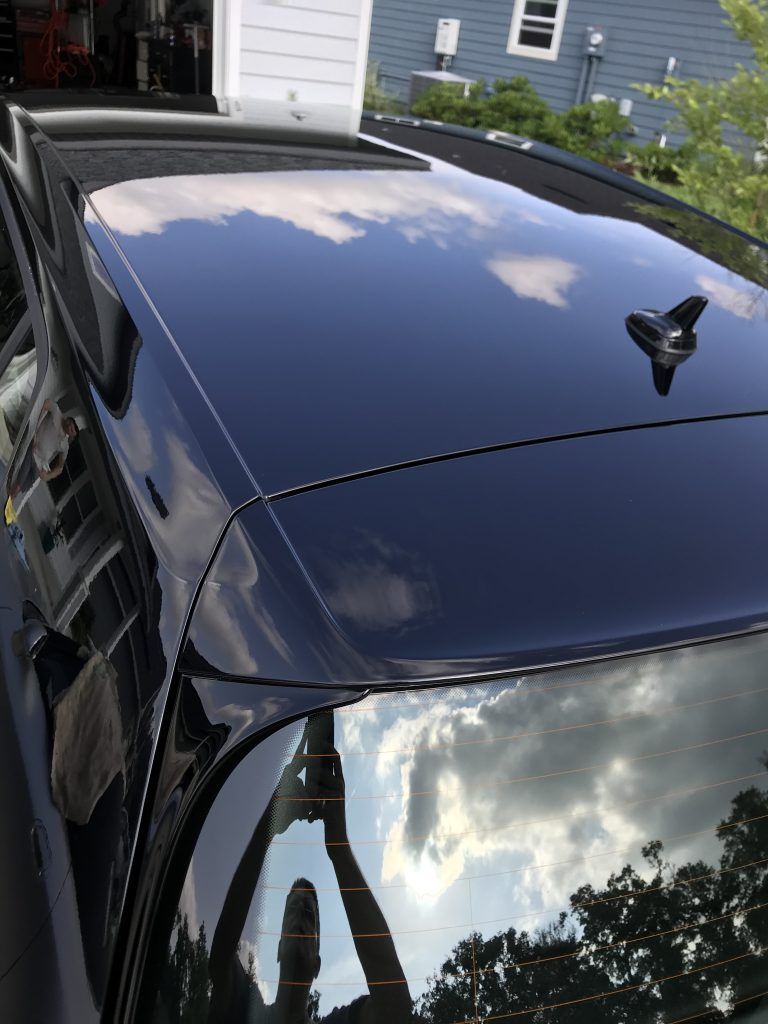 A black car with a roof antenna is parked in front of a house.