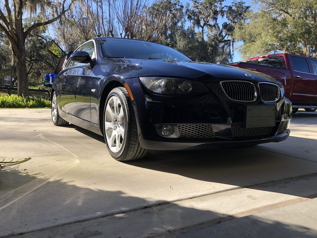 A black bmw is parked in a driveway next to a red truck.
