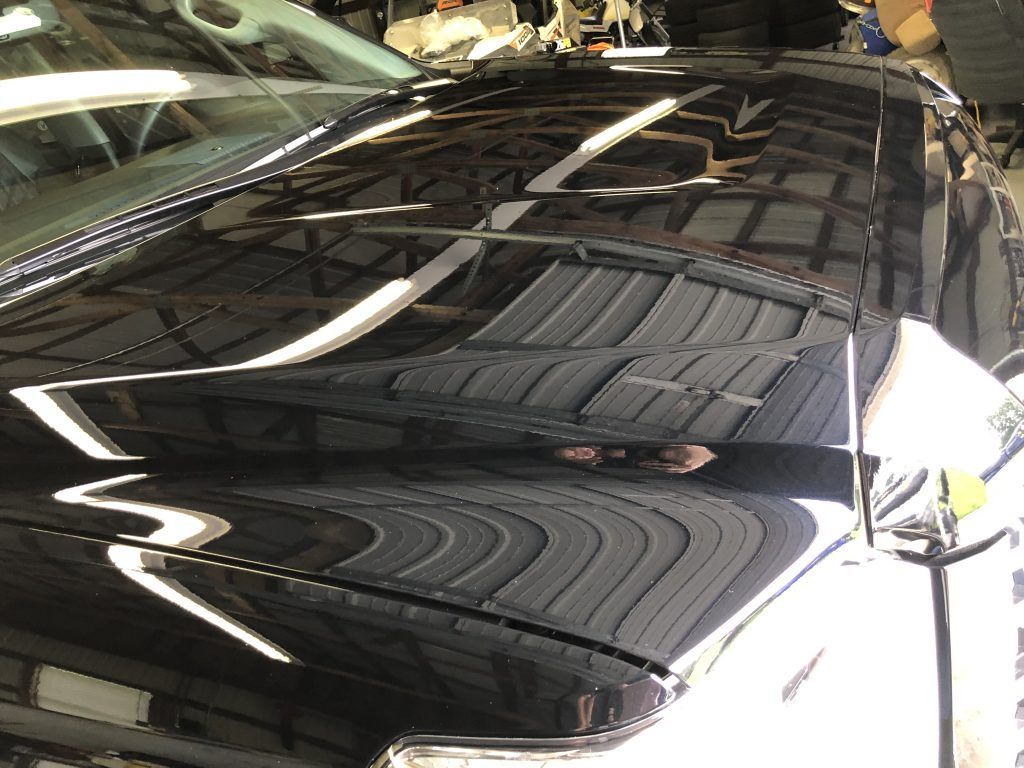 A black car with a shiny hood is parked in a garage.