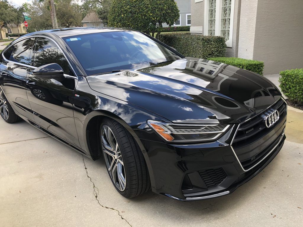 A black audi a7 is parked in a driveway in front of a house.