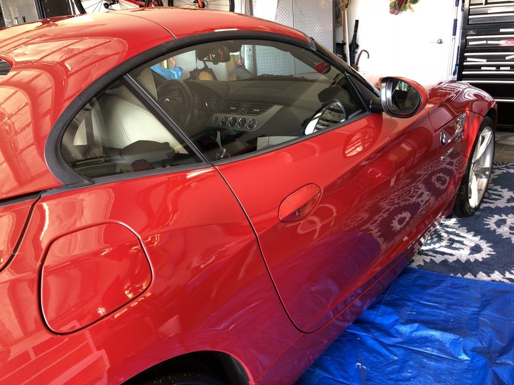 A red sports car is parked on a blue tarp in a garage.