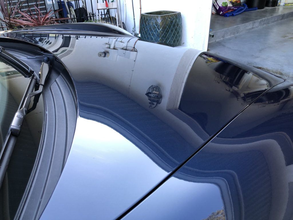 A close up of a car hood with a reflection of a building in it