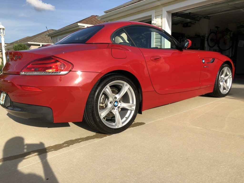 A red bmw z4 is parked in a driveway in front of a garage.