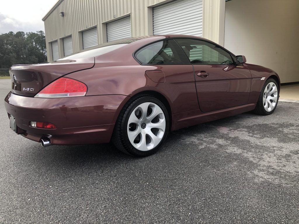 A maroon bmw 6 series coupe is parked in front of a building.