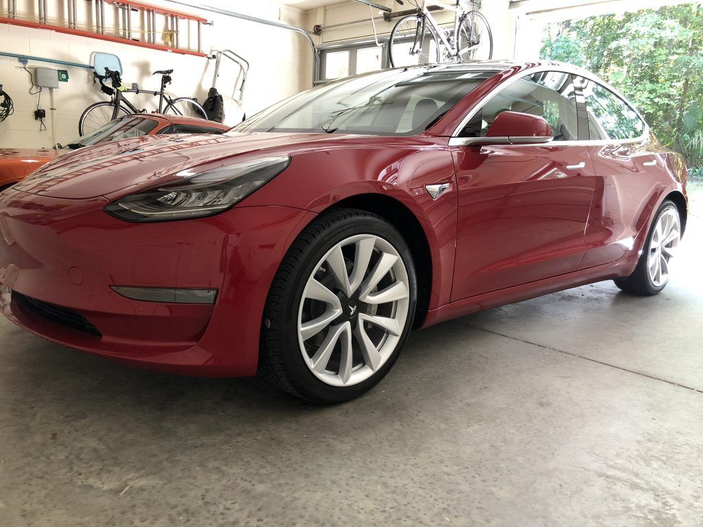 A red tesla model 3 is parked in a garage.