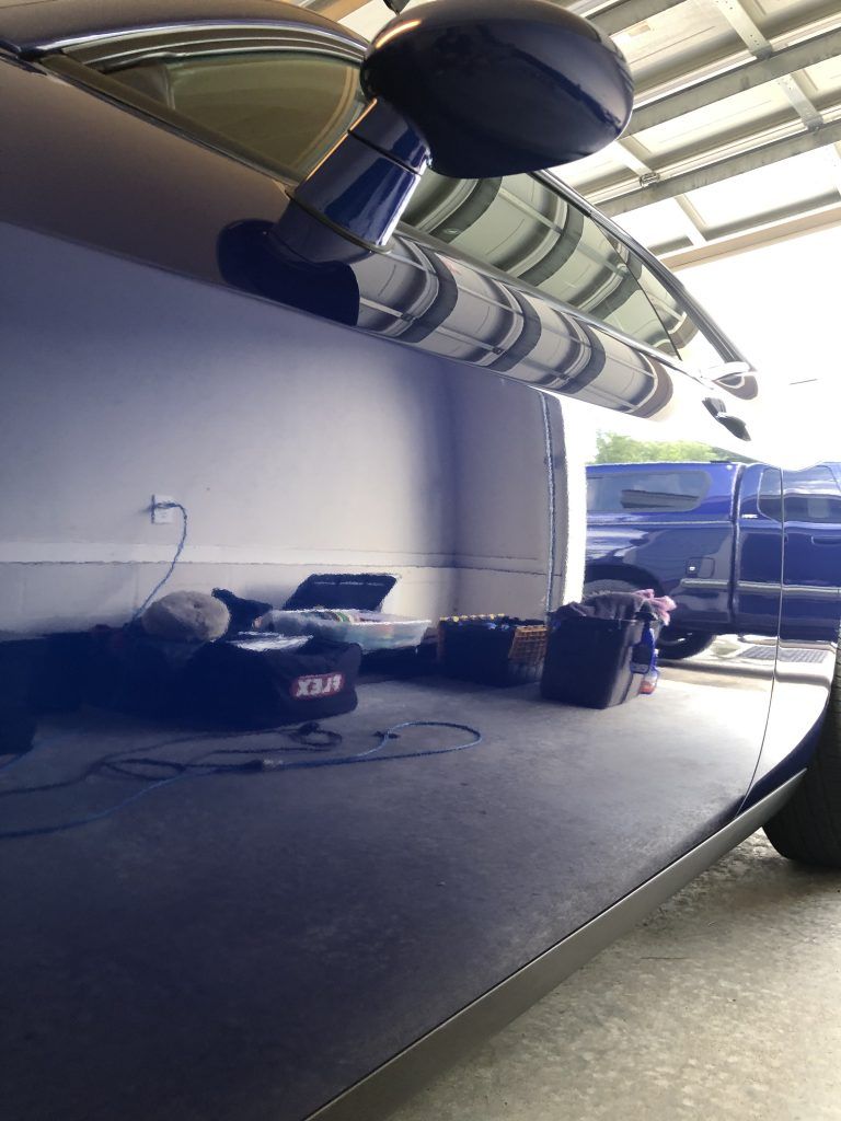 A blue car is parked in a garage next to a blue truck.