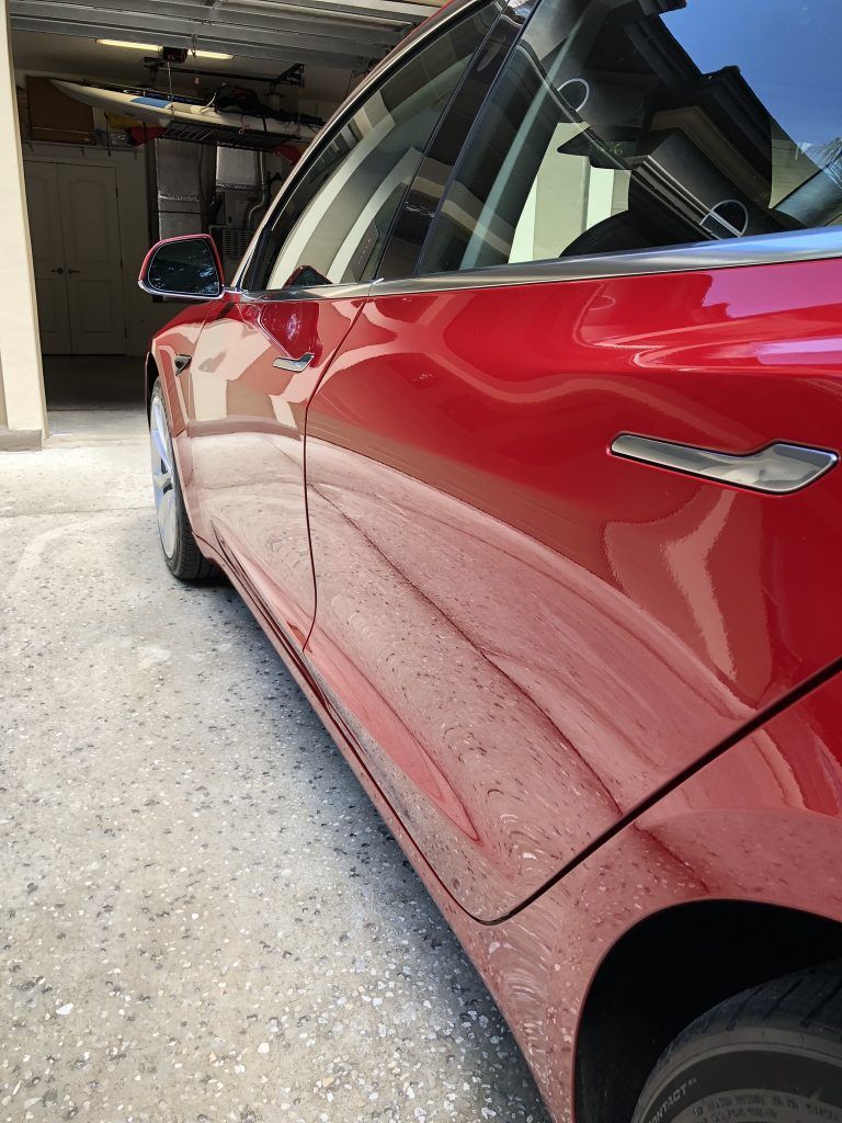 A red tesla model 3 is parked in a garage.