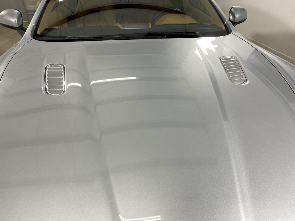 A close up of the hood of a silver car in a garage.
