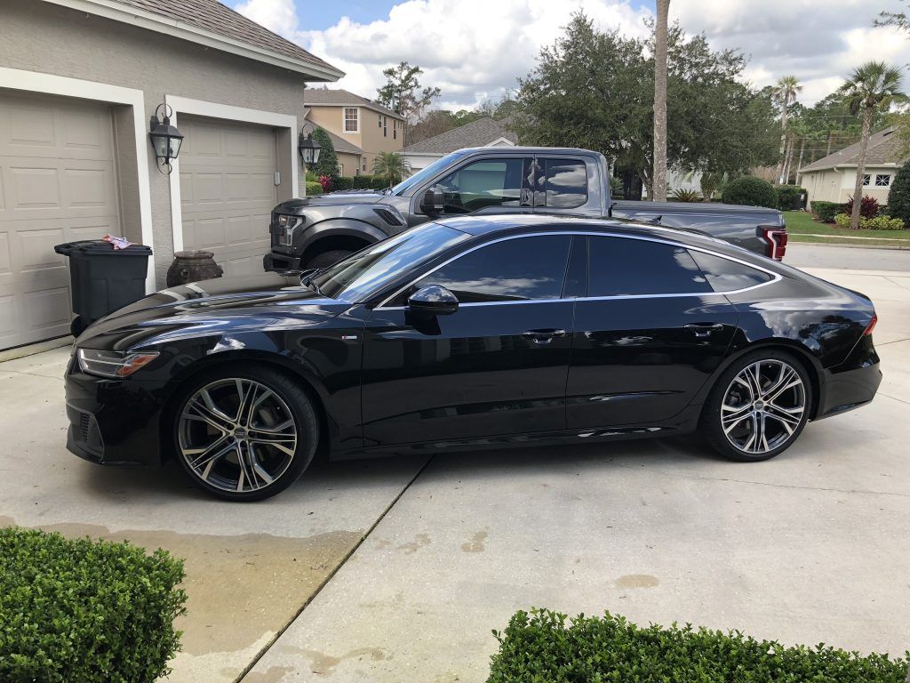 A black car is parked in a driveway next to a truck.