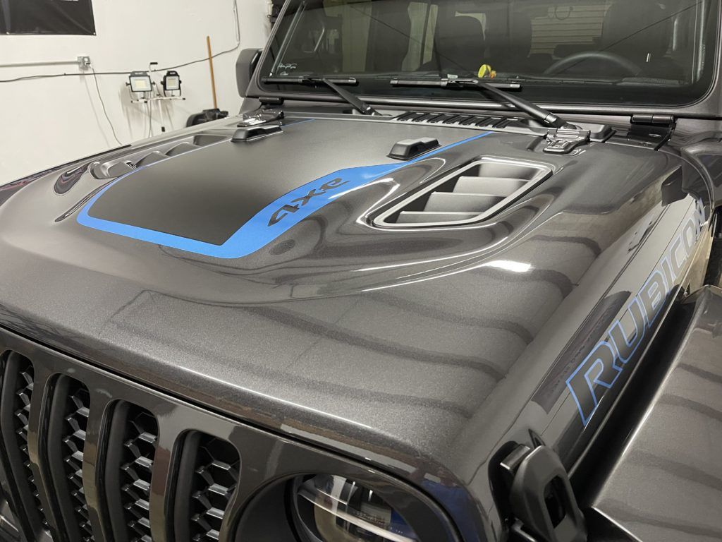 A black jeep with a blue stripe on the hood is parked in a garage.