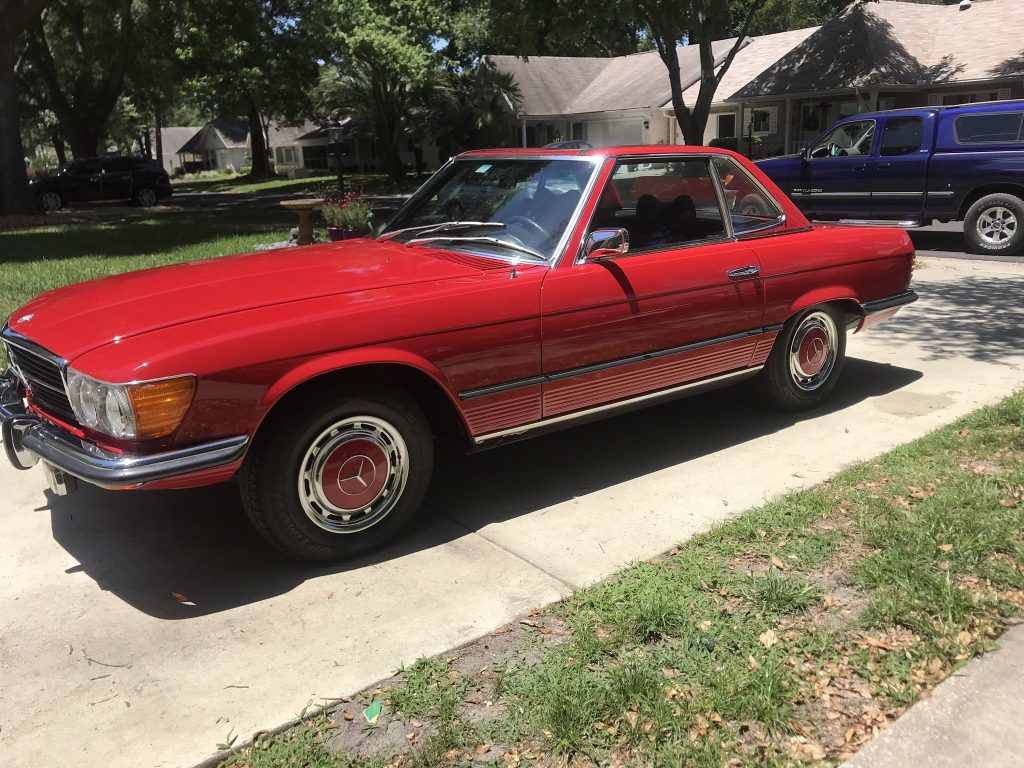 A red car is parked in a driveway next to a blue truck.