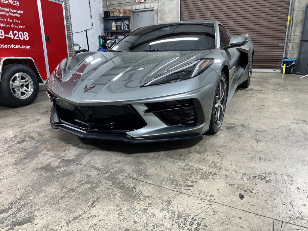 A gray sports car is parked in a garage next to a red trailer.