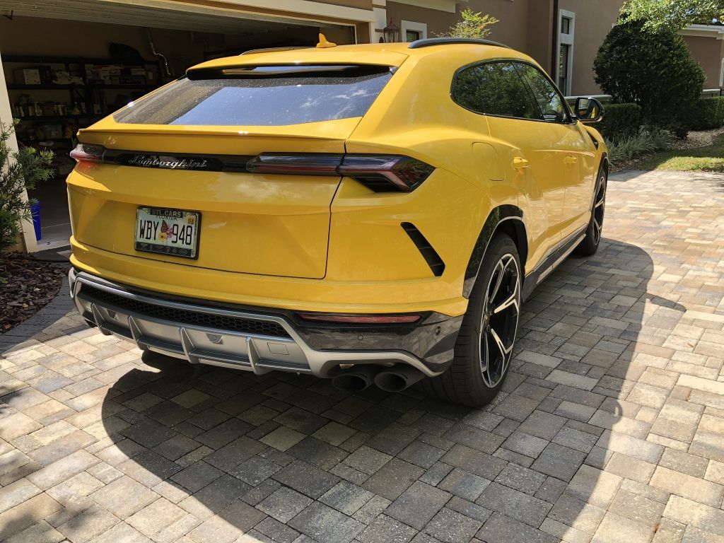 A yellow lamborghini urus is parked in a driveway.