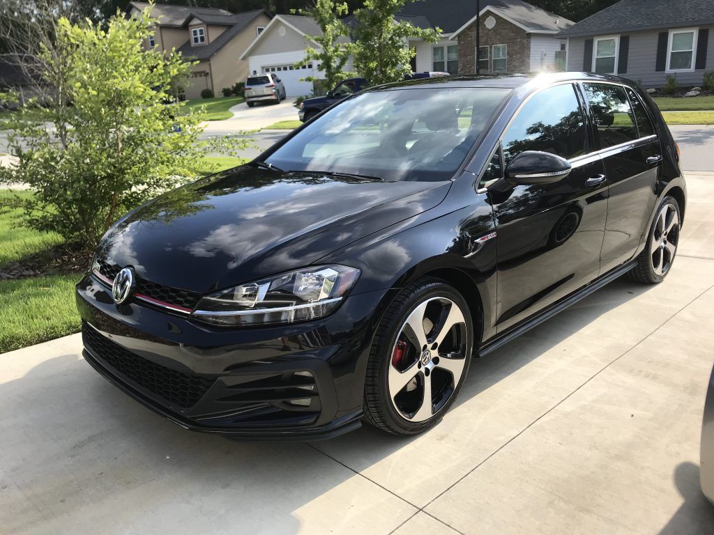 A black volkswagen golf gti is parked in a driveway in front of a house.