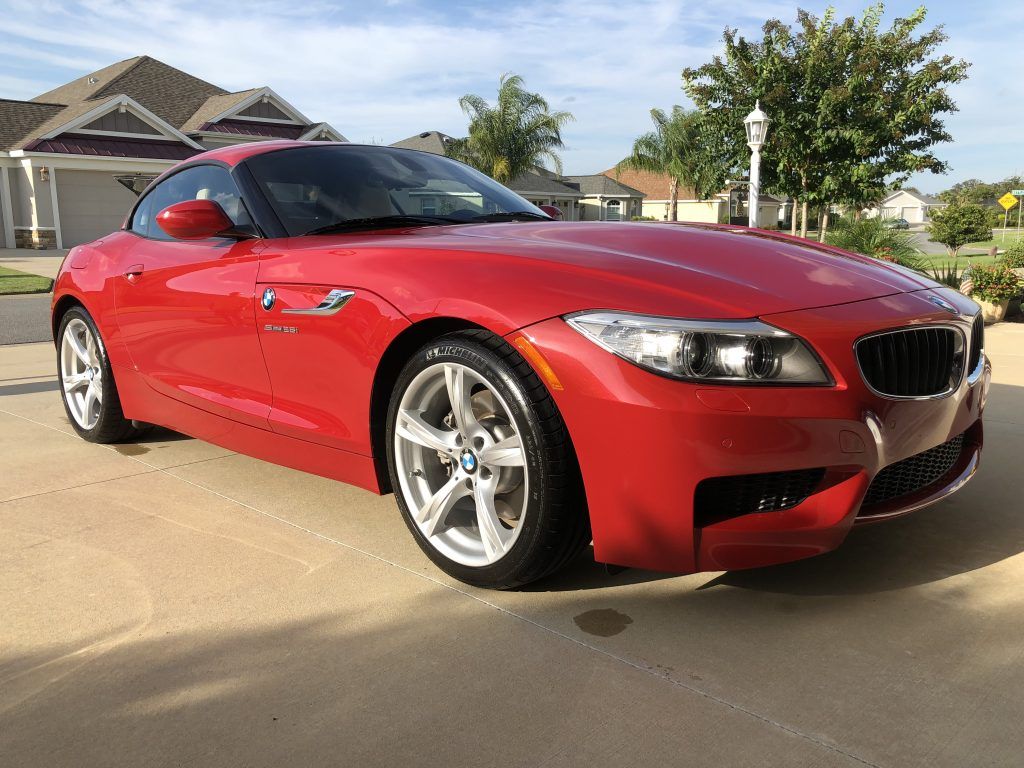 A red bmw z4 is parked in a driveway in front of a house.