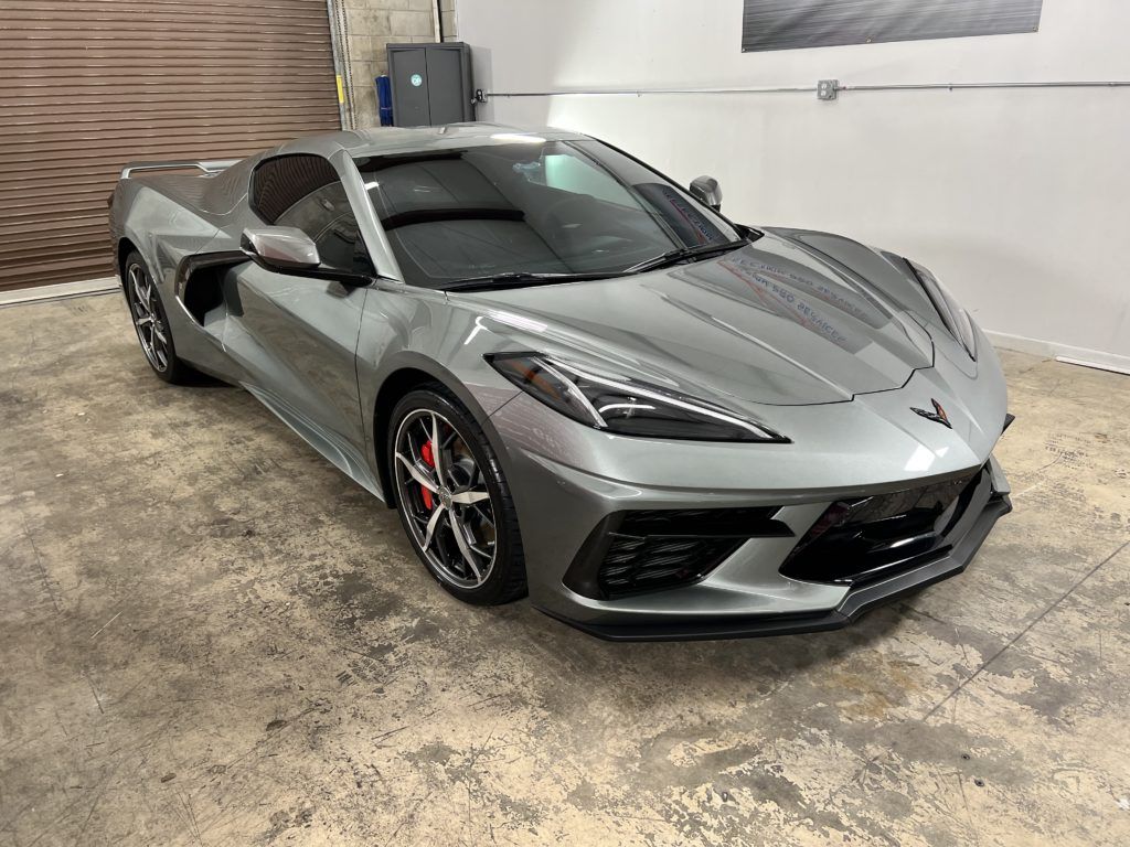 A gray corvette is parked in a garage next to a garage door.