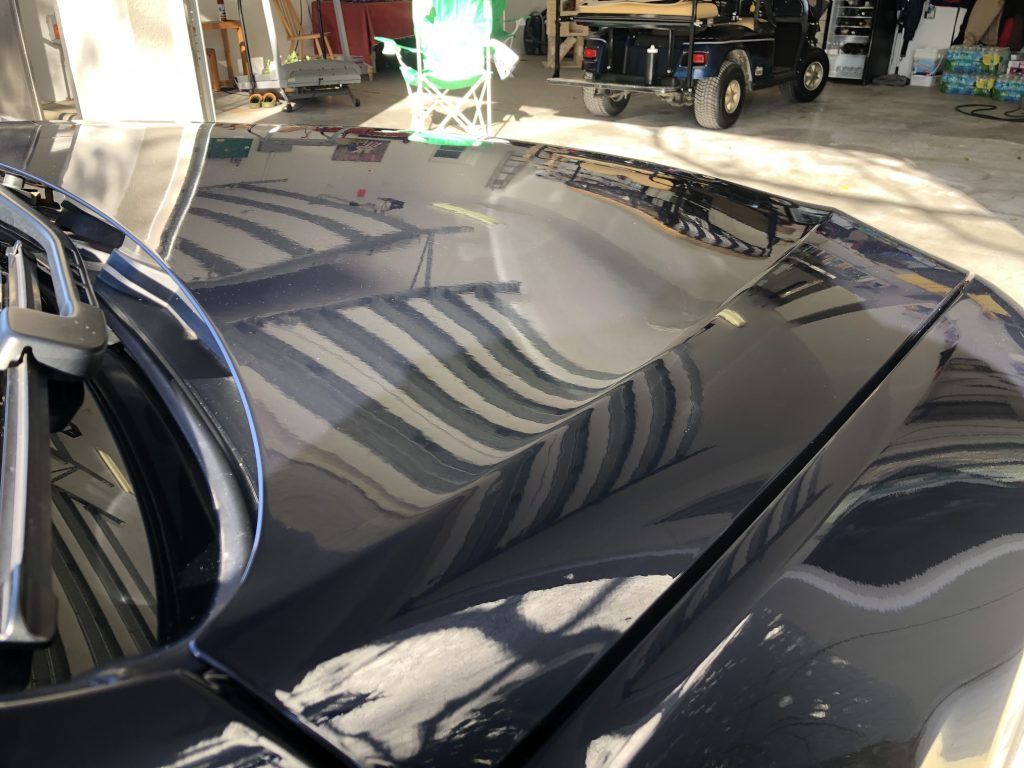 A black car is parked in a garage with a golf cart in the background.