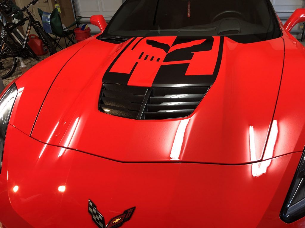 A red sports car with a checkered flag on the hood is parked in a garage.