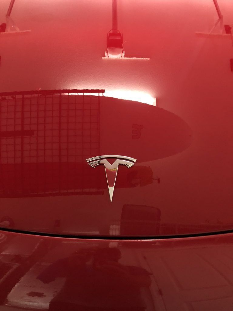 A red tesla model 3 is parked in a garage