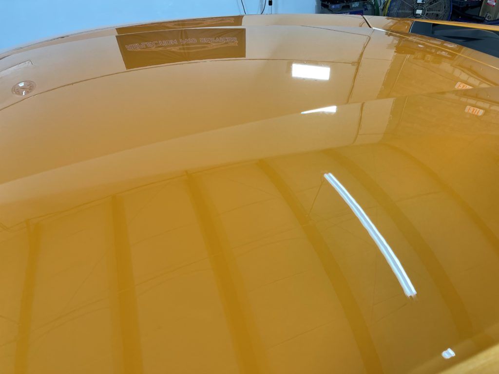 A close up of a yellow car 's hood in a garage.