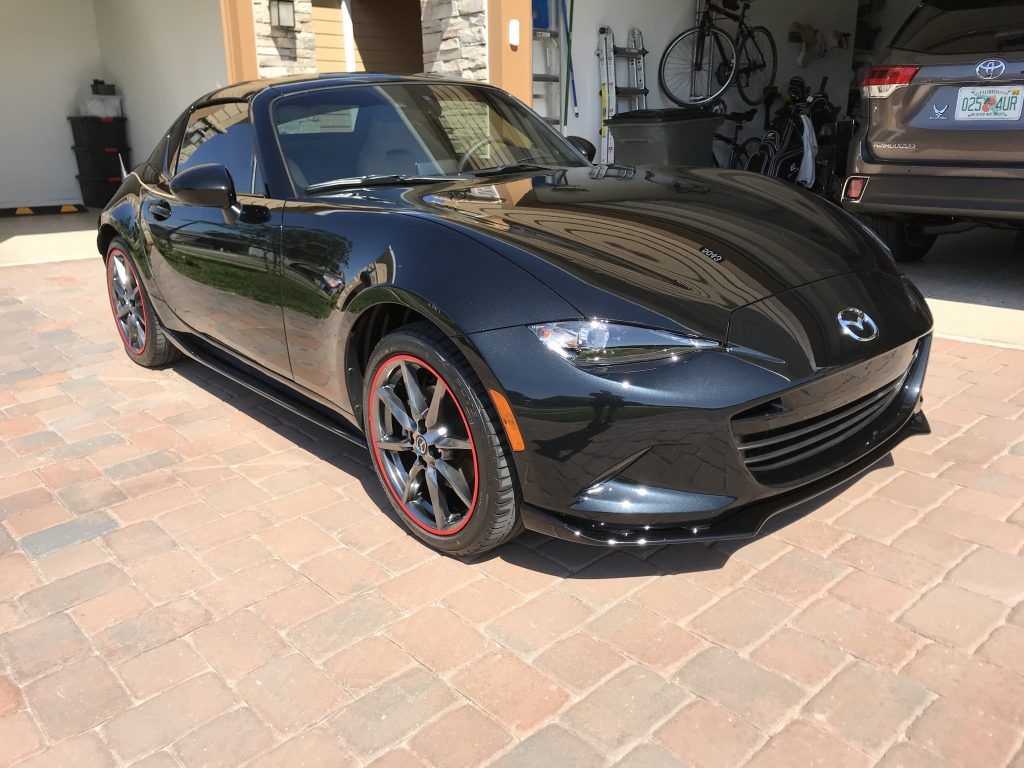 A black sports car is parked on a brick driveway in a garage.