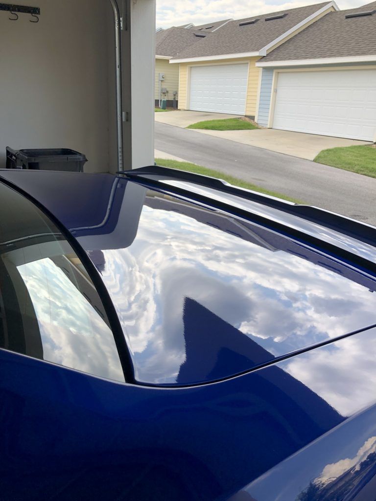 A blue car is parked in a garage with a reflection of clouds in the windshield.
