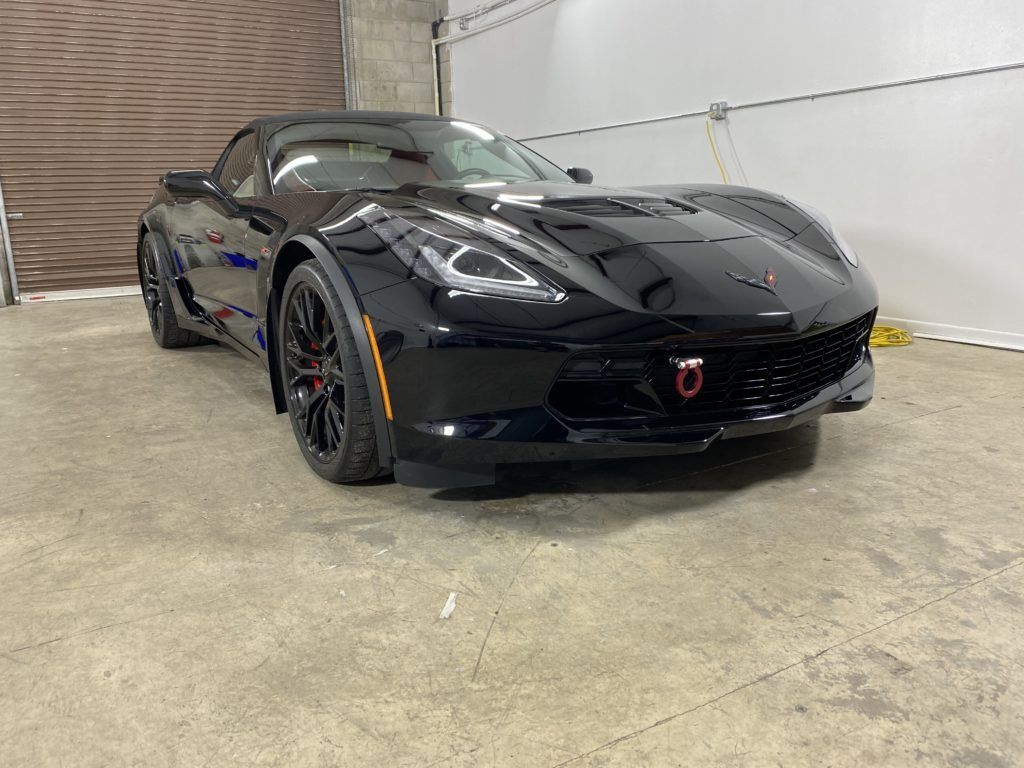 A black corvette is parked in a garage next to a garage door.