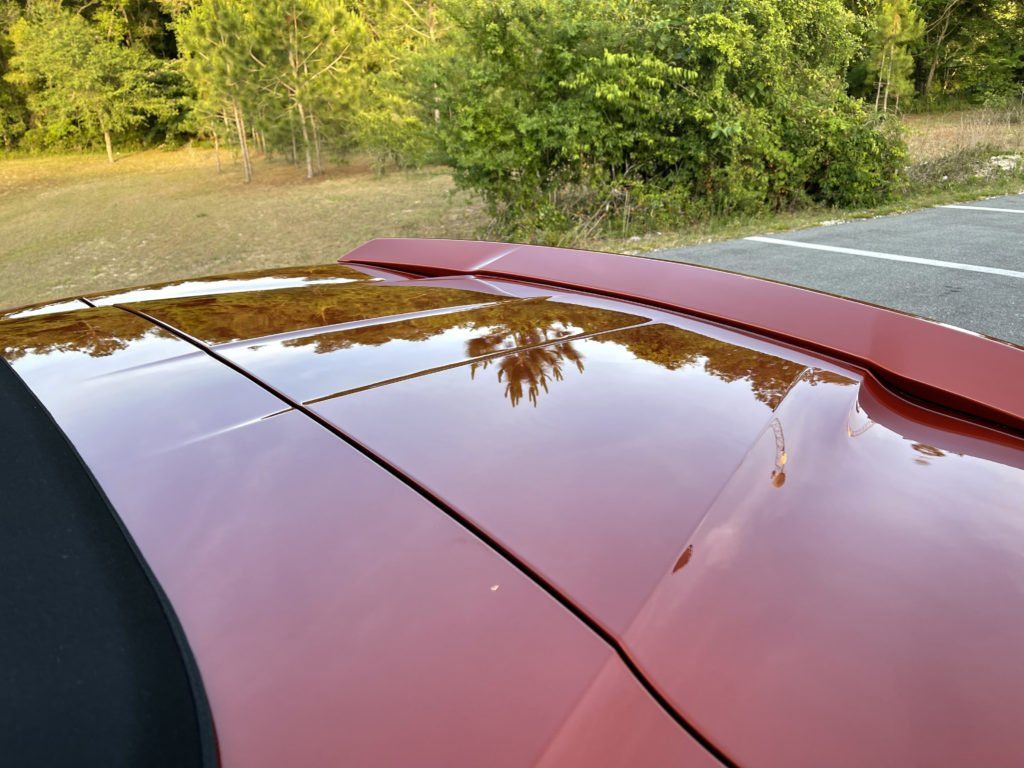 A red car is parked in a parking lot with trees in the background