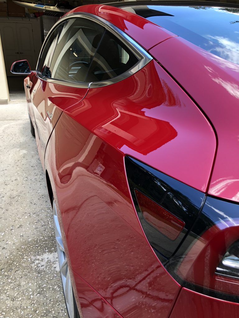 A red tesla model 3 is parked in a driveway.