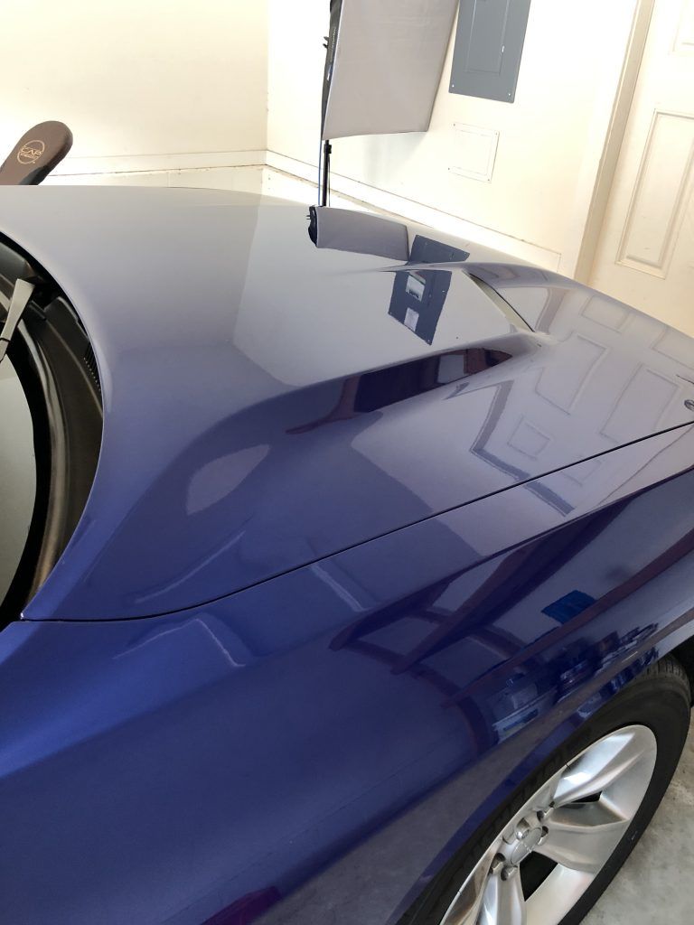 A blue car is parked in a garage with the hood up.