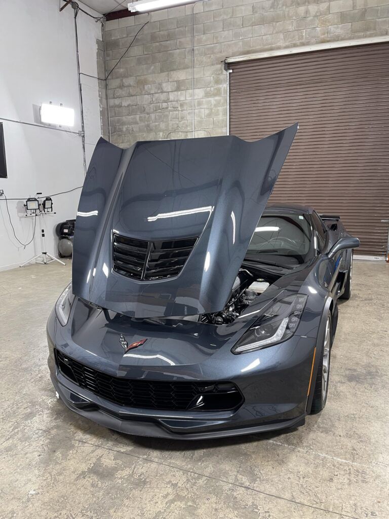 A gray corvette with its hood up is parked in a garage.