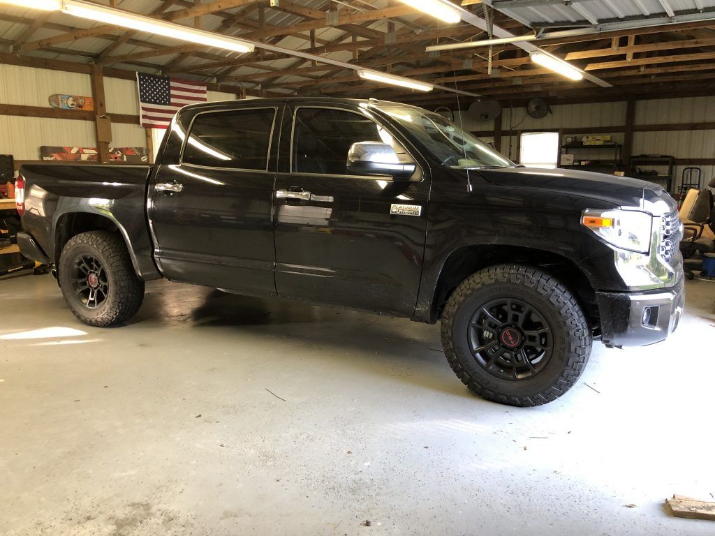 A black truck is parked in a garage next to an american flag.