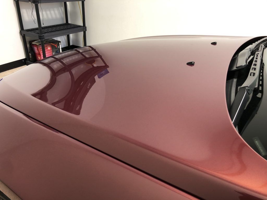 The hood of a red car is sitting in a garage.