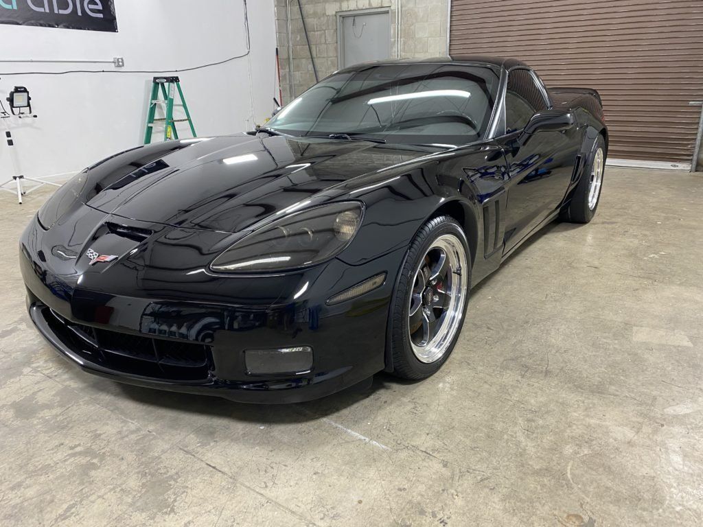 A black corvette is parked in a garage next to a ladder.