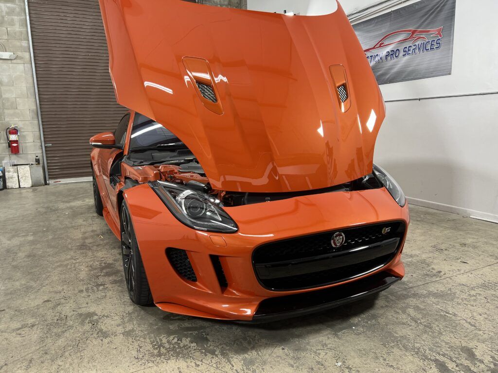 An orange sports car with the hood up is parked in a garage.