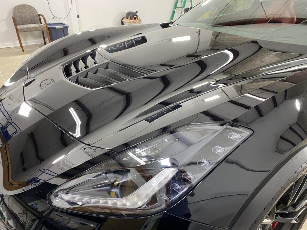 A close up of a black car 's hood and headlight in a garage.