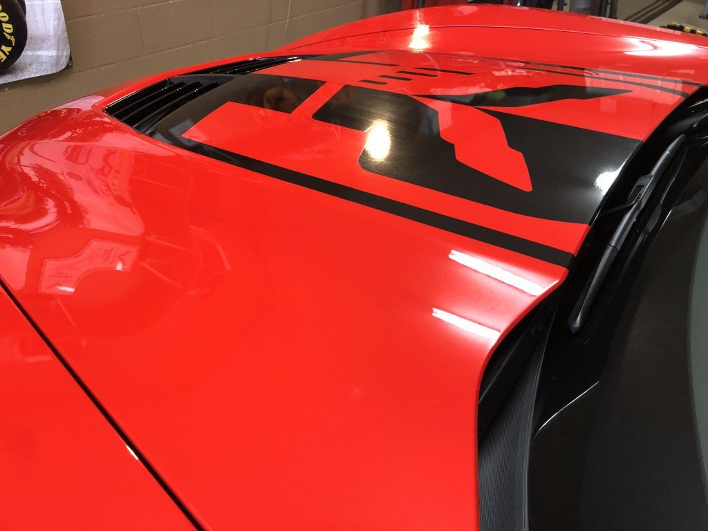 A red car with a black stripe on the hood is parked in a garage.