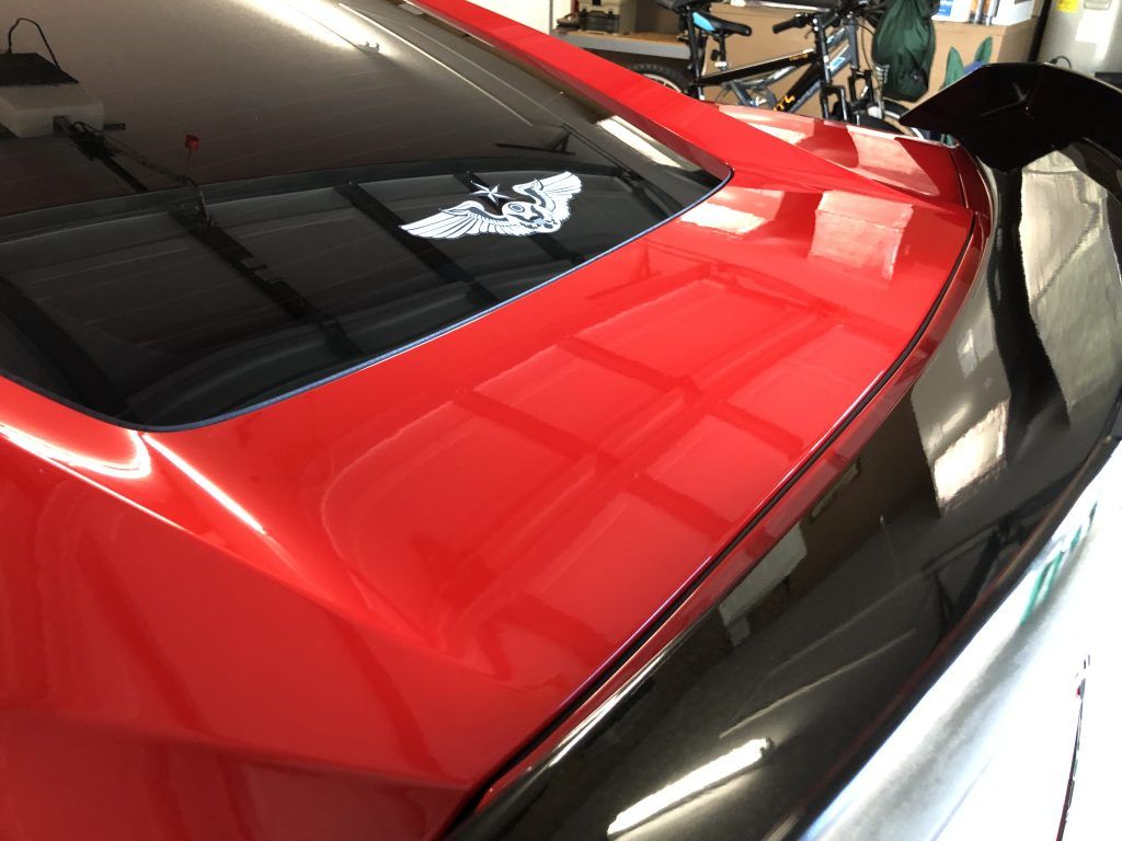 A red car with a black spoiler is parked in a garage