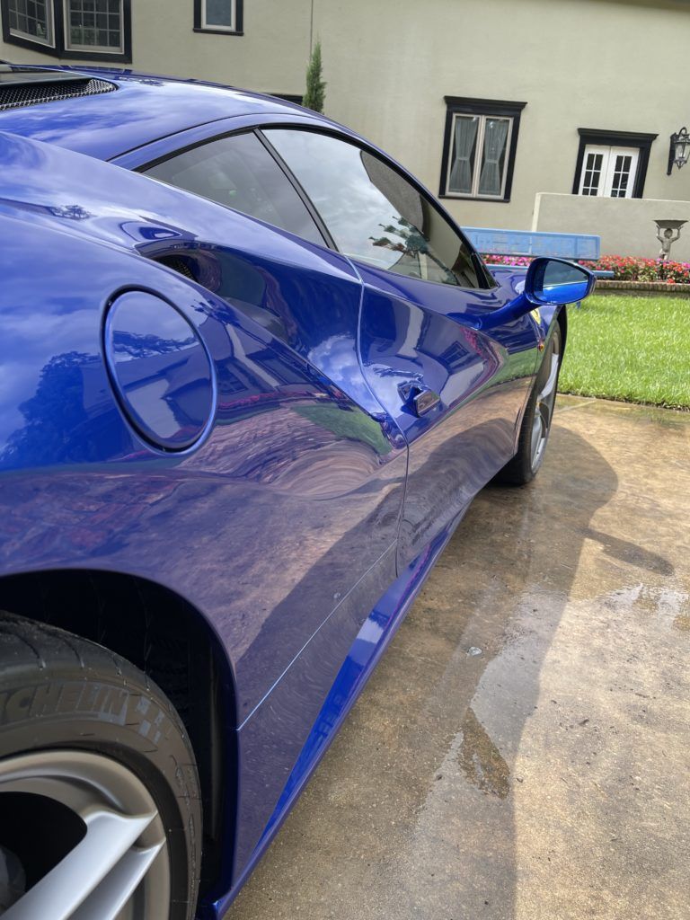 A blue sports car is parked in a driveway in front of a house.