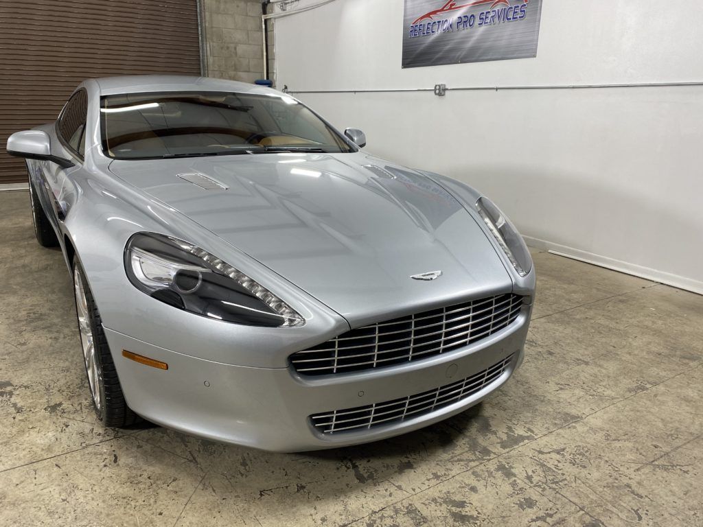 A silver aston martin sports car is parked in a garage.