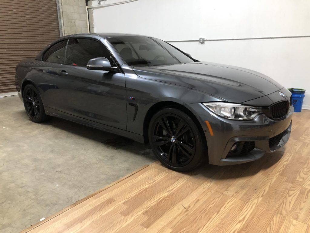 A gray bmw is parked in a garage next to a garage door.