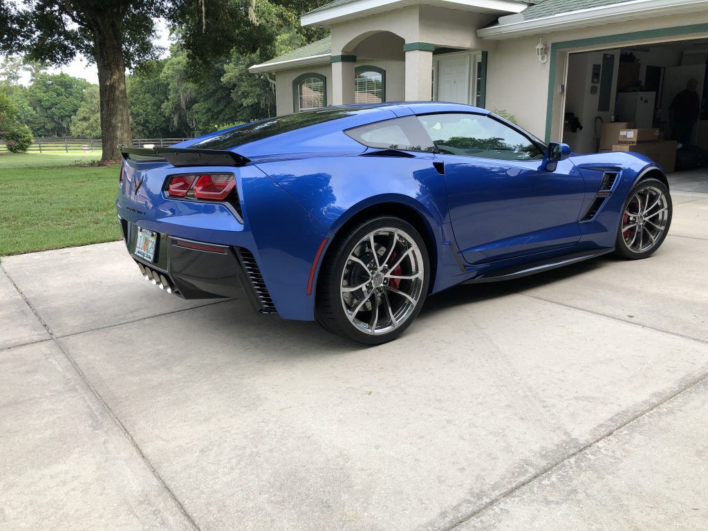 A blue sports car is parked in a driveway in front of a house.