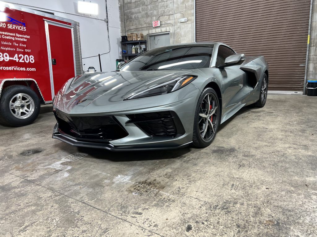 A gray sports car is parked in a garage next to a red trailer.
