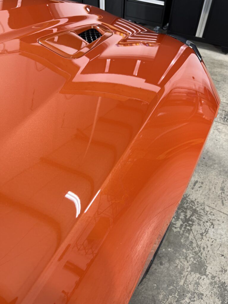 A close up of the hood of an orange car in a garage.