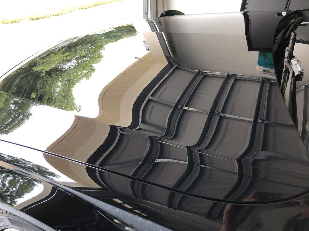 A black car is parked in a garage with a reflection of trees in the windshield.