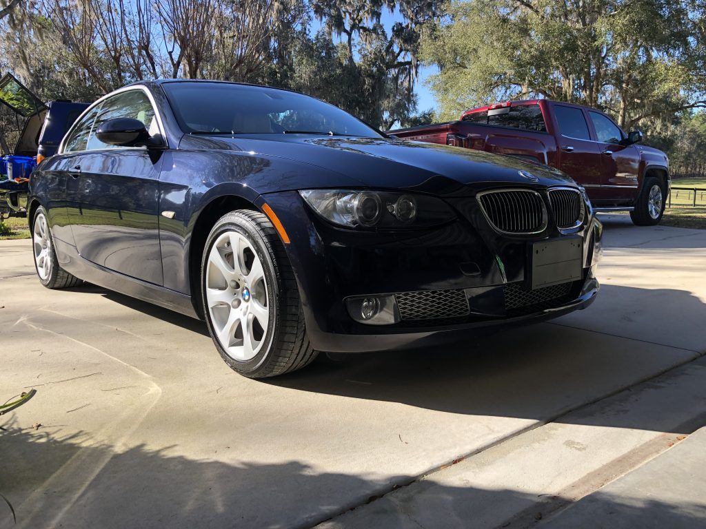 A black bmw is parked in a driveway next to a red truck.